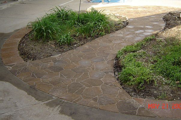 Brown stone-patterned concrete pathway with garden beds on either side.