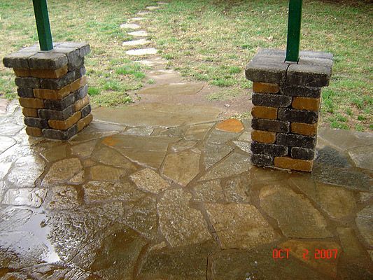 Stone patio with two brick pillars and a flagstone path, wet from rain.