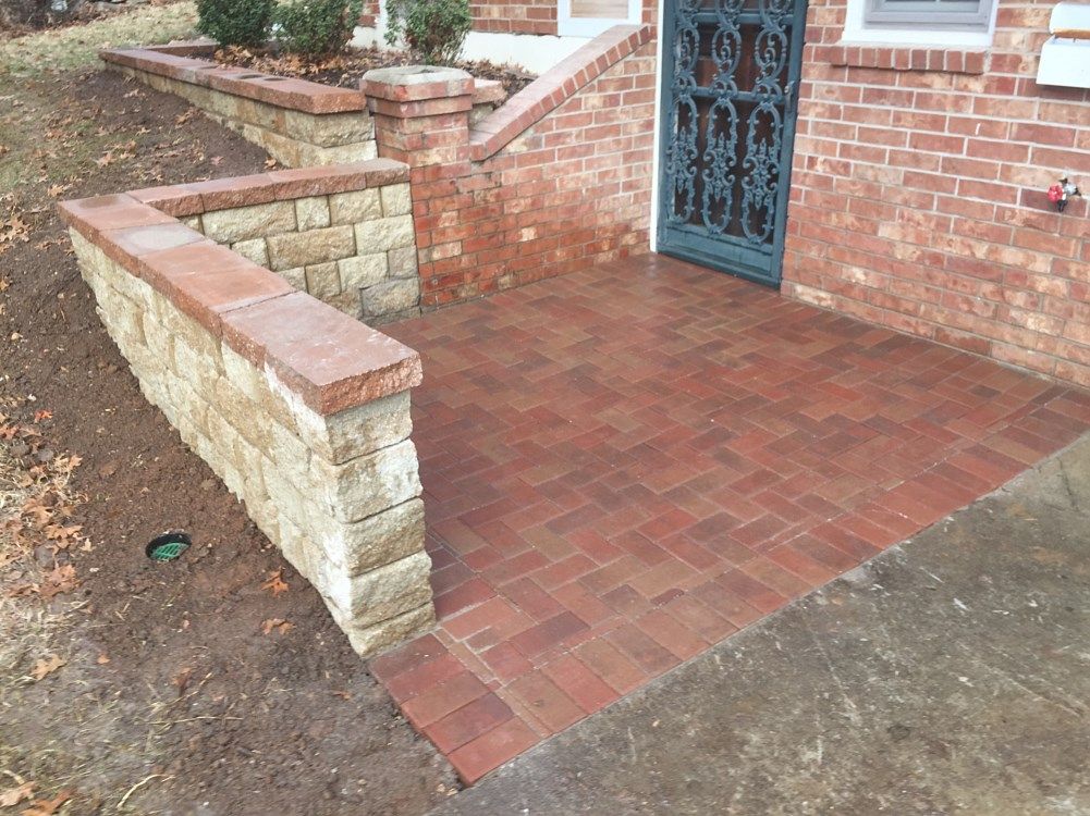 Brick patio with retaining wall, leading to a front door with ornate black metal security bars.
