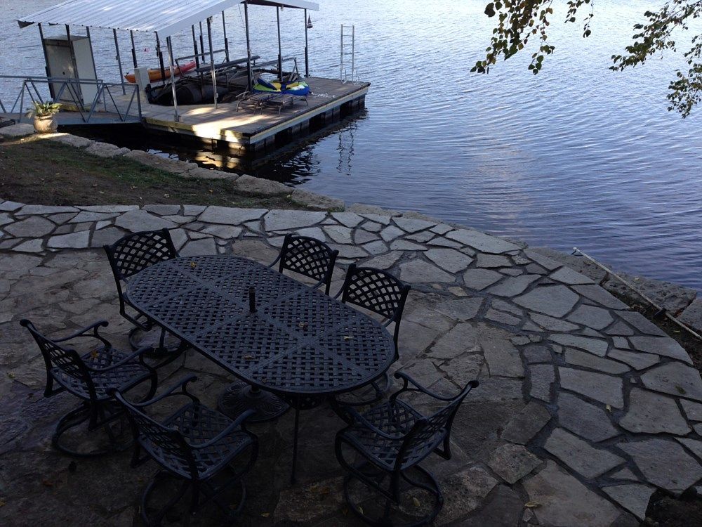 Patio overlooking a lake with a dock; stone patio, metal table and chairs.