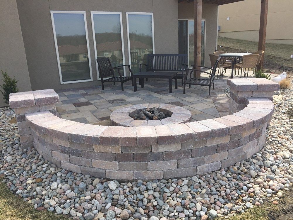 Stone patio with built-in fire pit and seating area, surrounded by a low brick wall and landscaping.