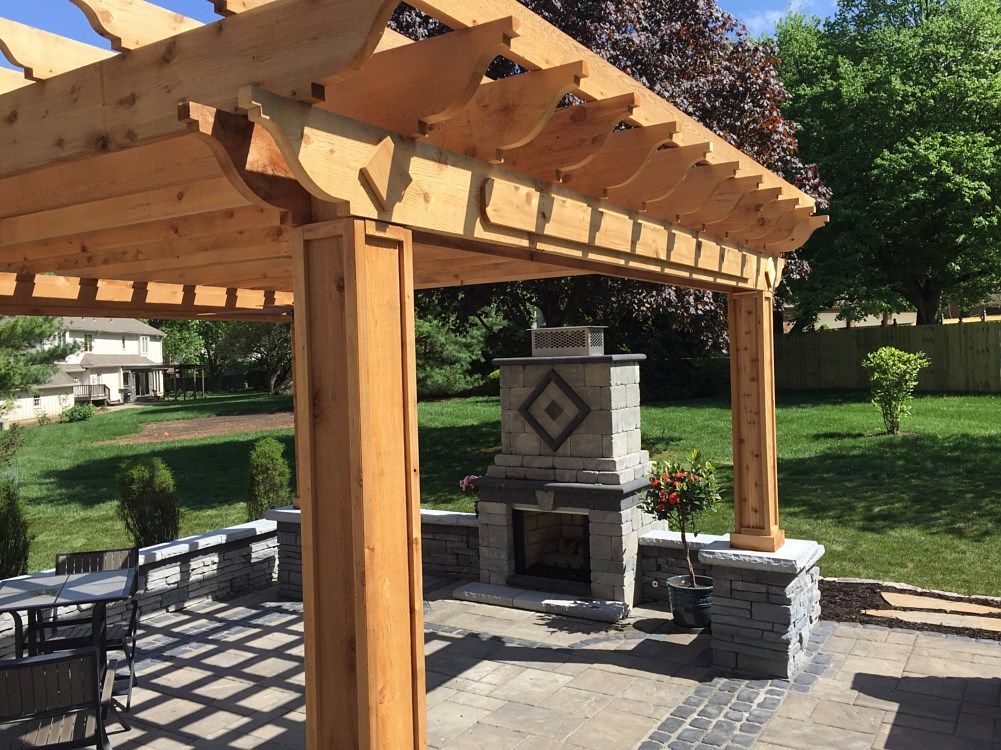 Wooden pergola over patio with fireplace and backyard.