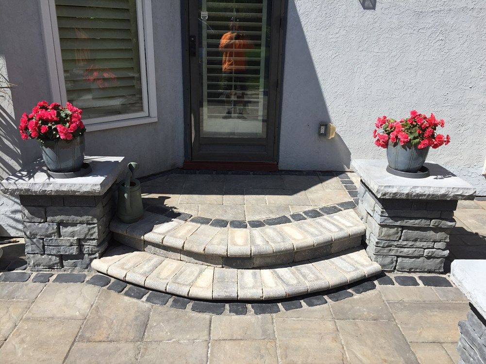 Stone steps leading to a door, with potted red flowers on stone pillars.