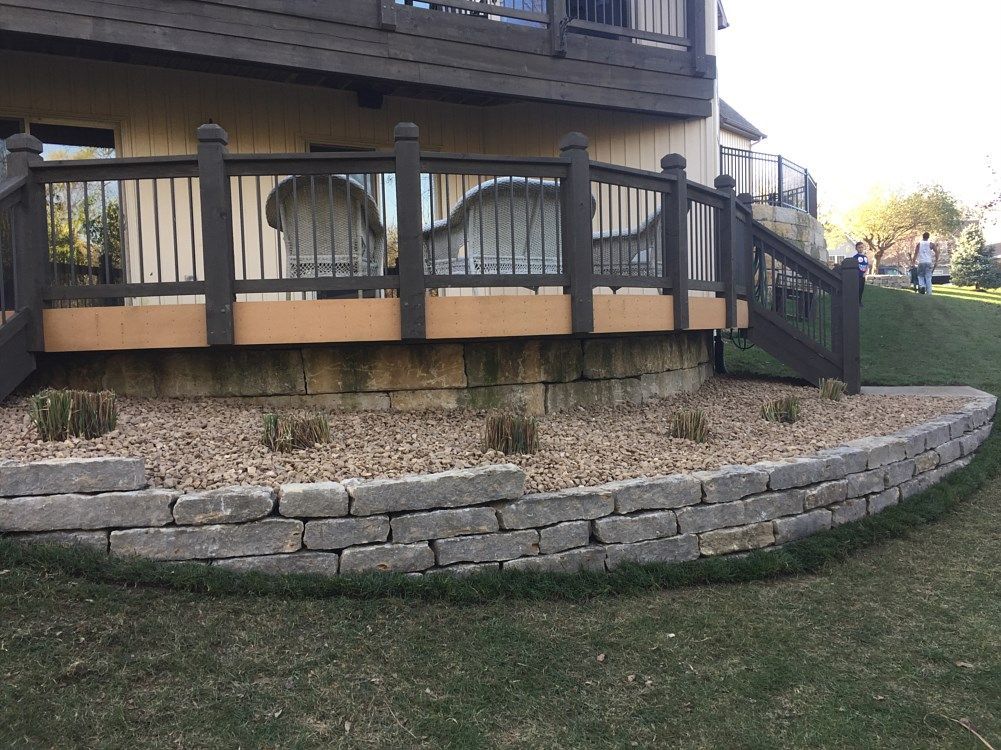 Deck with stone retaining wall, seating, and landscaping; outdoors.