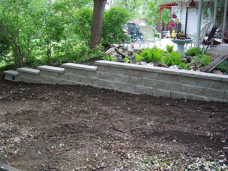 Retaining wall made of gray blocks in a backyard, surrounding a garden bed.