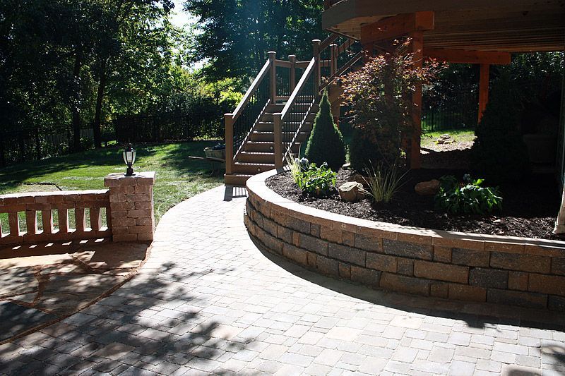 A curved brick retaining wall with a paved path, stairs, and a small garden, outside.