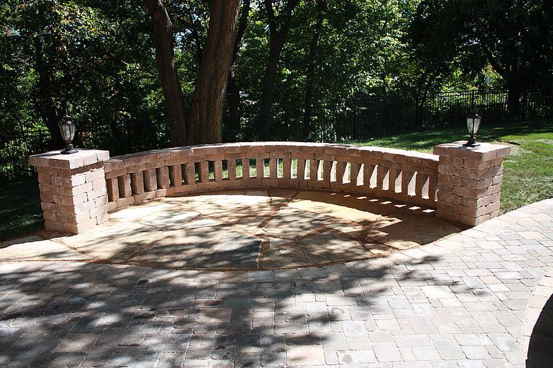 Curved brick patio with decorative railing and lamp posts, in a wooded area.