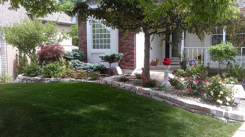 Lush green lawn slopes up to a landscaped yard with a brick-faced house, trees, and flowers.