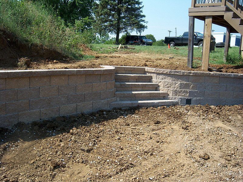 Stone retaining wall with steps leading up, in a yard under construction.