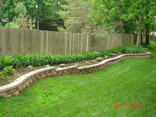 A retaining wall in a backyard, holding a planted garden bed along a wooden fence.