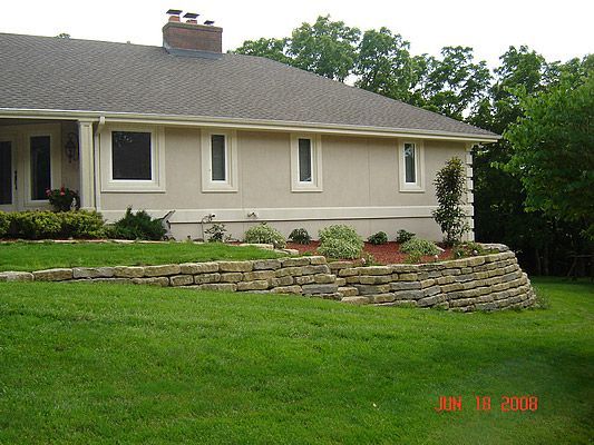 Tan house with stone retaining wall and small landscaping.