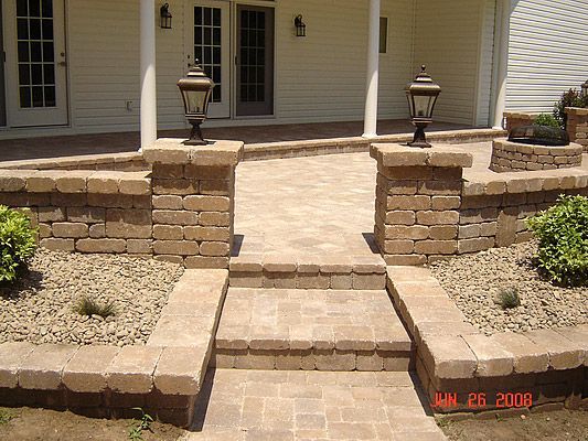 Brick pathway with steps, pillars, and landscaping leading to a porch with doors.