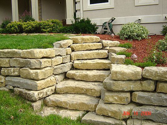 Stone steps built into a hillside, bordered by grass and mulch with plants.