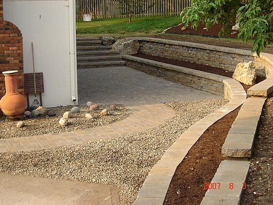 Stone patio and retaining walls in a backyard, brown and beige tones.