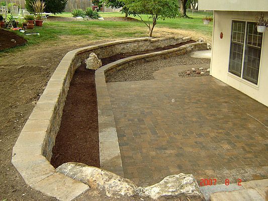 Stone retaining walls with mulch beds and a concrete patio.