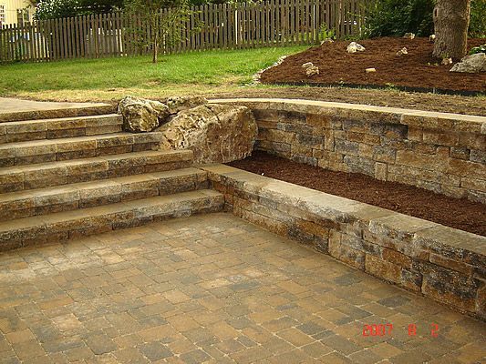 Stone patio with steps, retaining wall, and mulch bed.