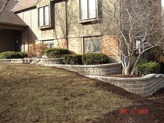 Stone retaining walls with shrubs in front of a house.