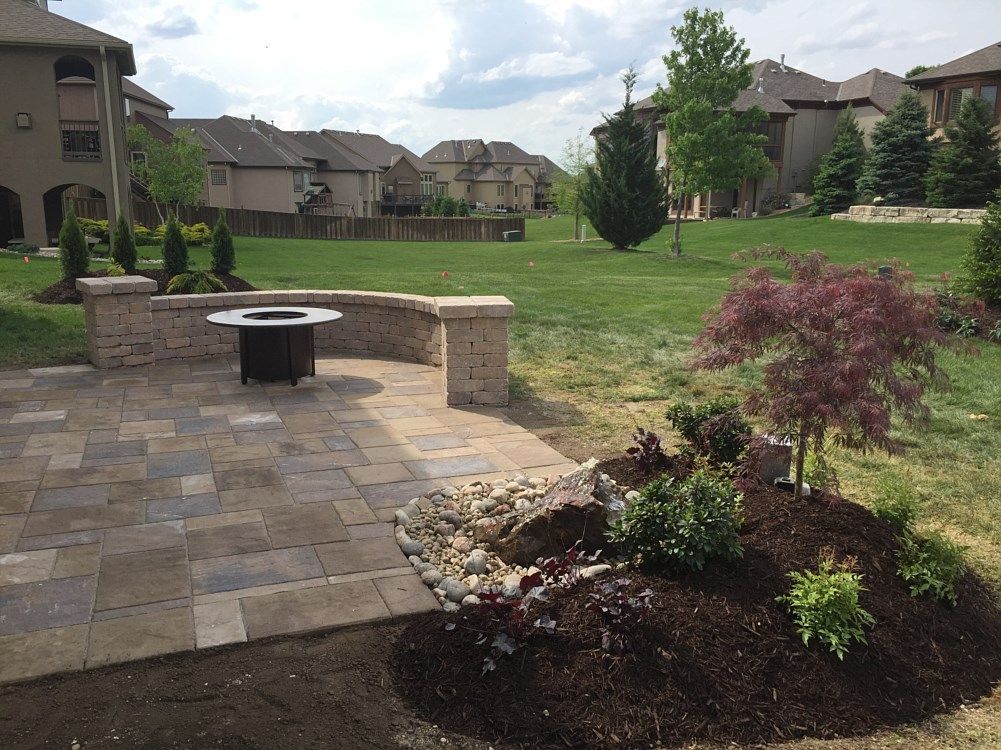Patio with fire pit, stone wall, and landscaping in a backyard setting.