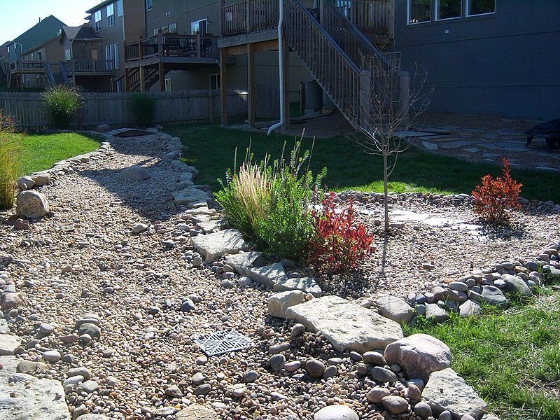 Rock garden with gravel pathway, bordered by rocks, leading to grassy areas with shrubs and trees.