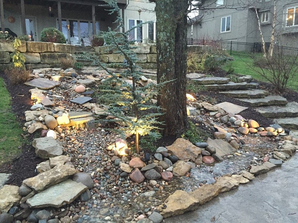 Stone landscape with a small water feature, rocks, tree, steps, and soft lighting.