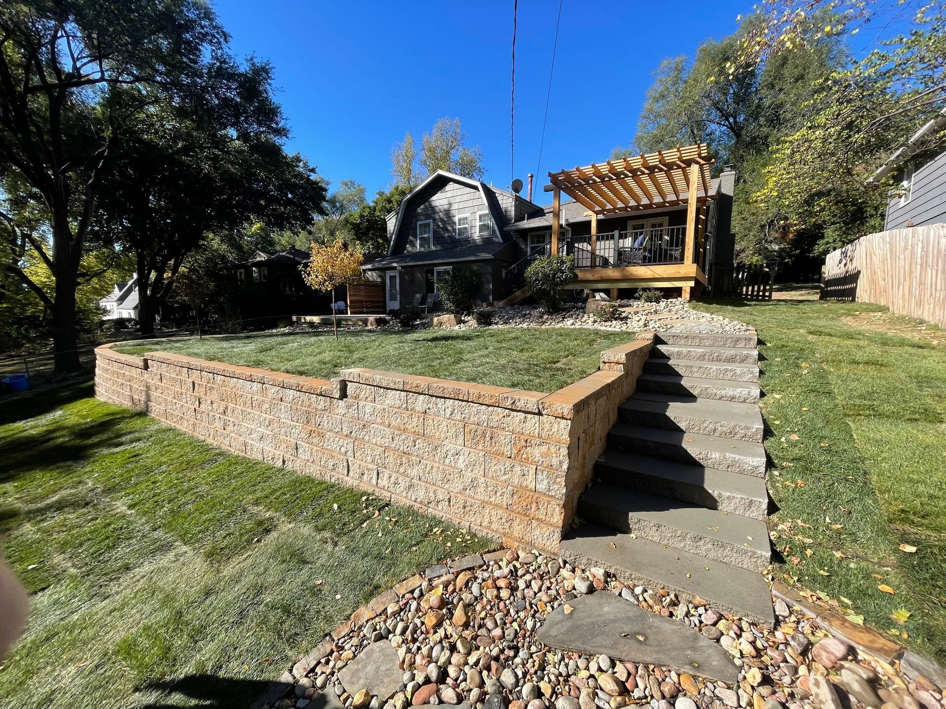Stone retaining wall and steps leading to a wooden deck on a sunny landscaped hillside yard