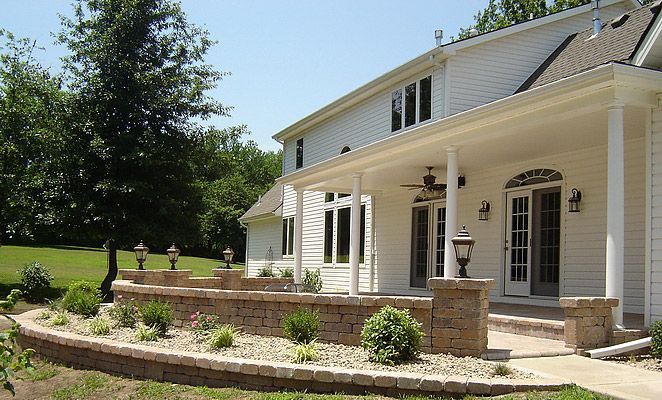 House with a porch and brick retaining wall, green lawn, sunny day.