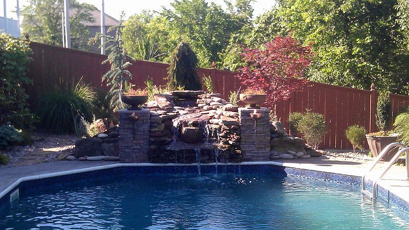 Pool with a stone waterfall feature, surrounded by landscaping and a wooden fence.