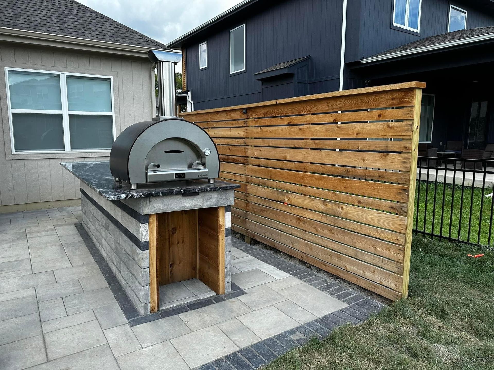 Outdoor brick patio with a built-in pizza oven beside a wooden privacy fence