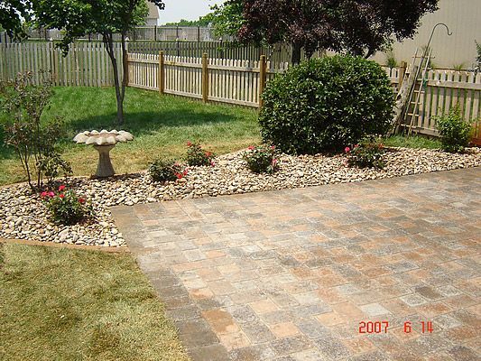 Brick patio with garden bed and birdbath, bordered by a wooden fence.