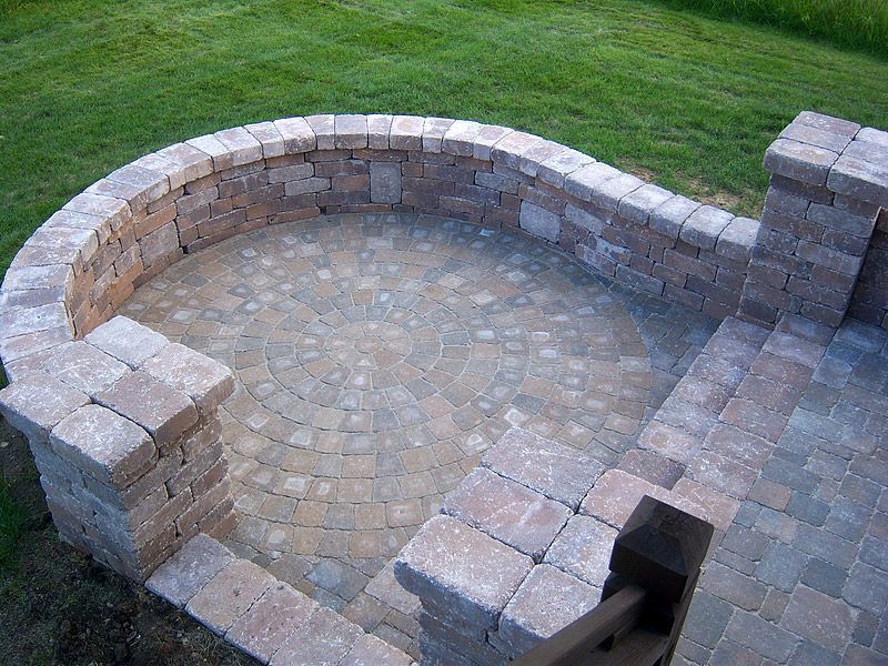 Brick patio with curved wall and step down to another level, surrounded by grass.