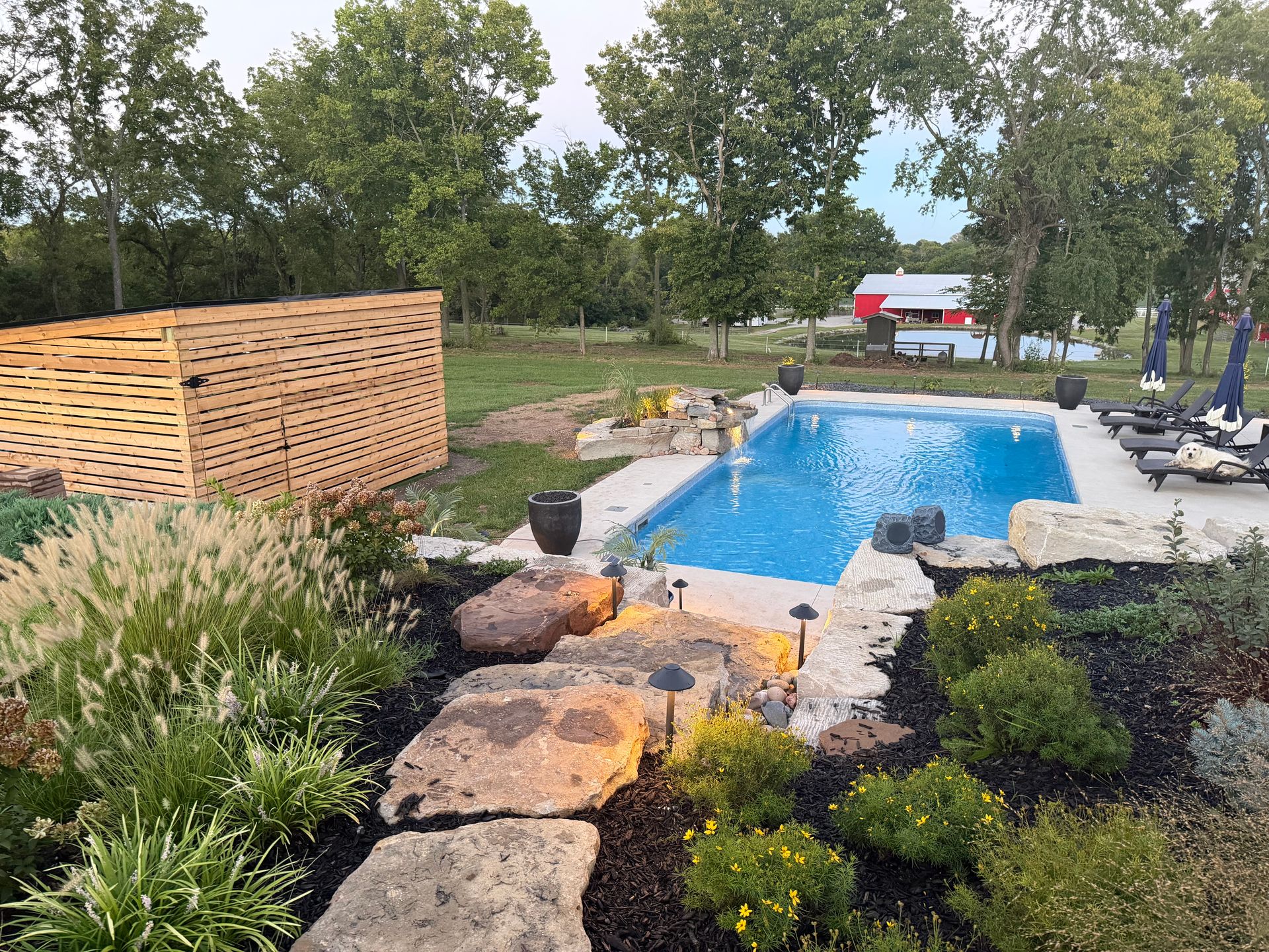 Backyard pool with stone path, landscaping, lounge chairs, and a red-roofed gazebo in the distance