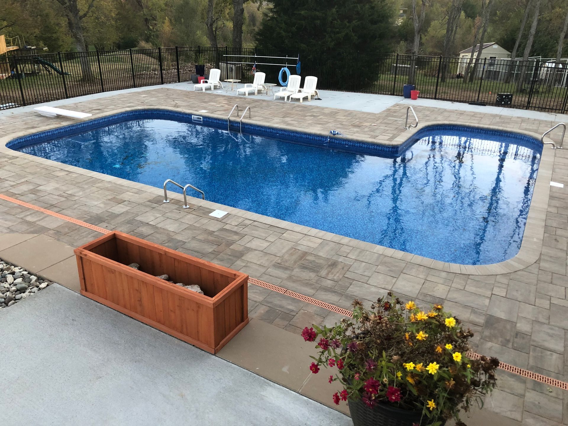 Backyard swimming pool with blue water, patio pavers, lounge chairs, and flower planters