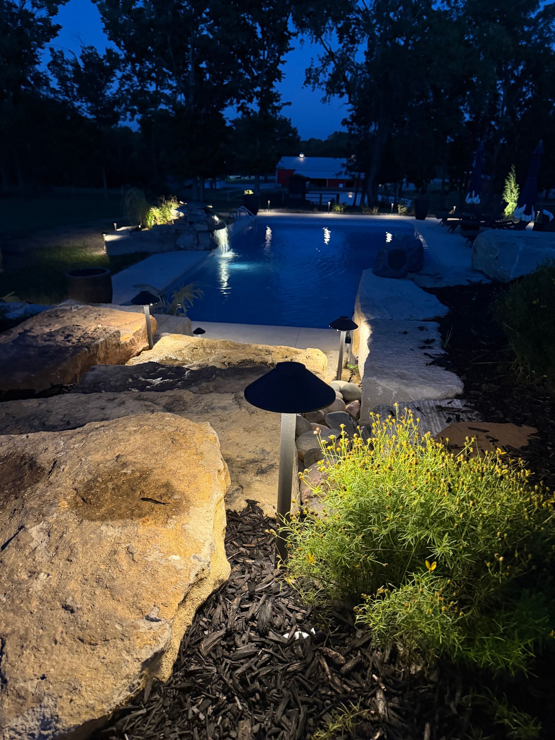 Nighttime garden path with illuminated rocks, mushroom lights, and a pool reflecting lights.