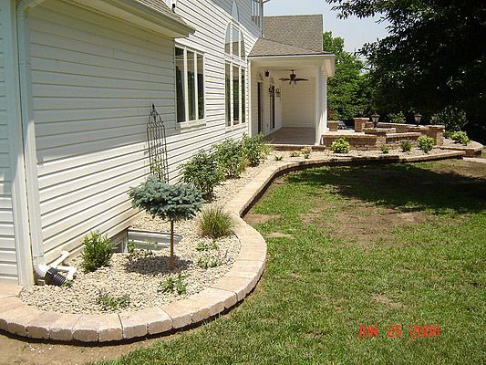 House exterior with landscaping including brick borders, shrubs, and a patio.