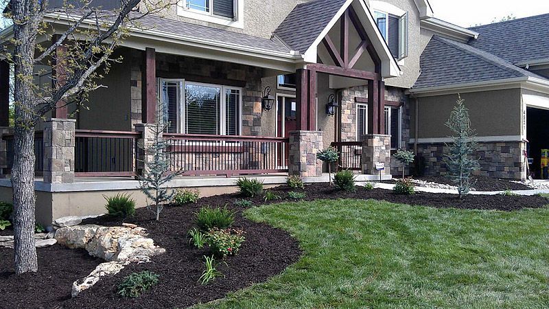 House exterior with stone and wood accents, landscaped yard with mulch, grass, and bushes.