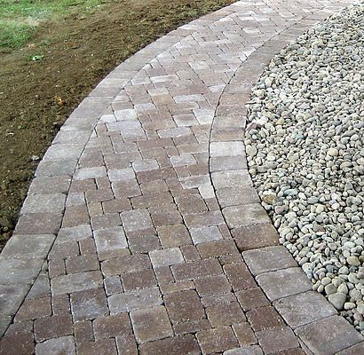 Stone paver walkway curves through gravel, bordered by grass on one side.