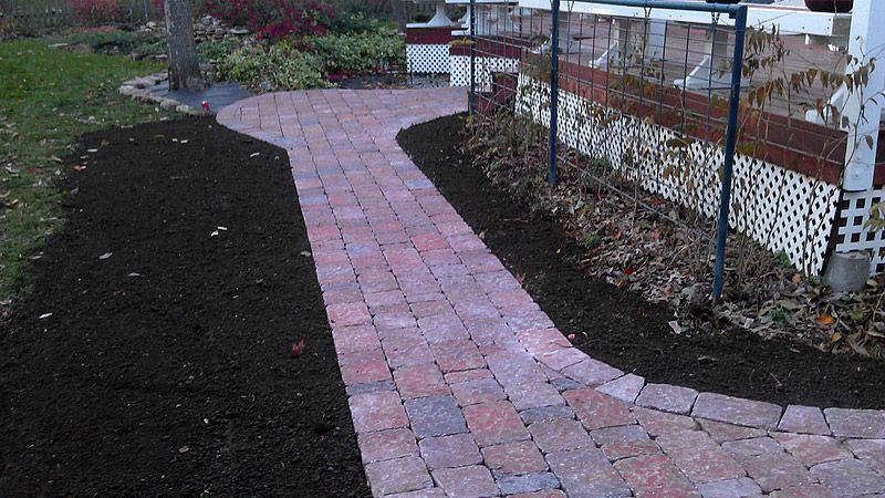 Brick pathway curving through yard, bordered by fresh dark mulch.