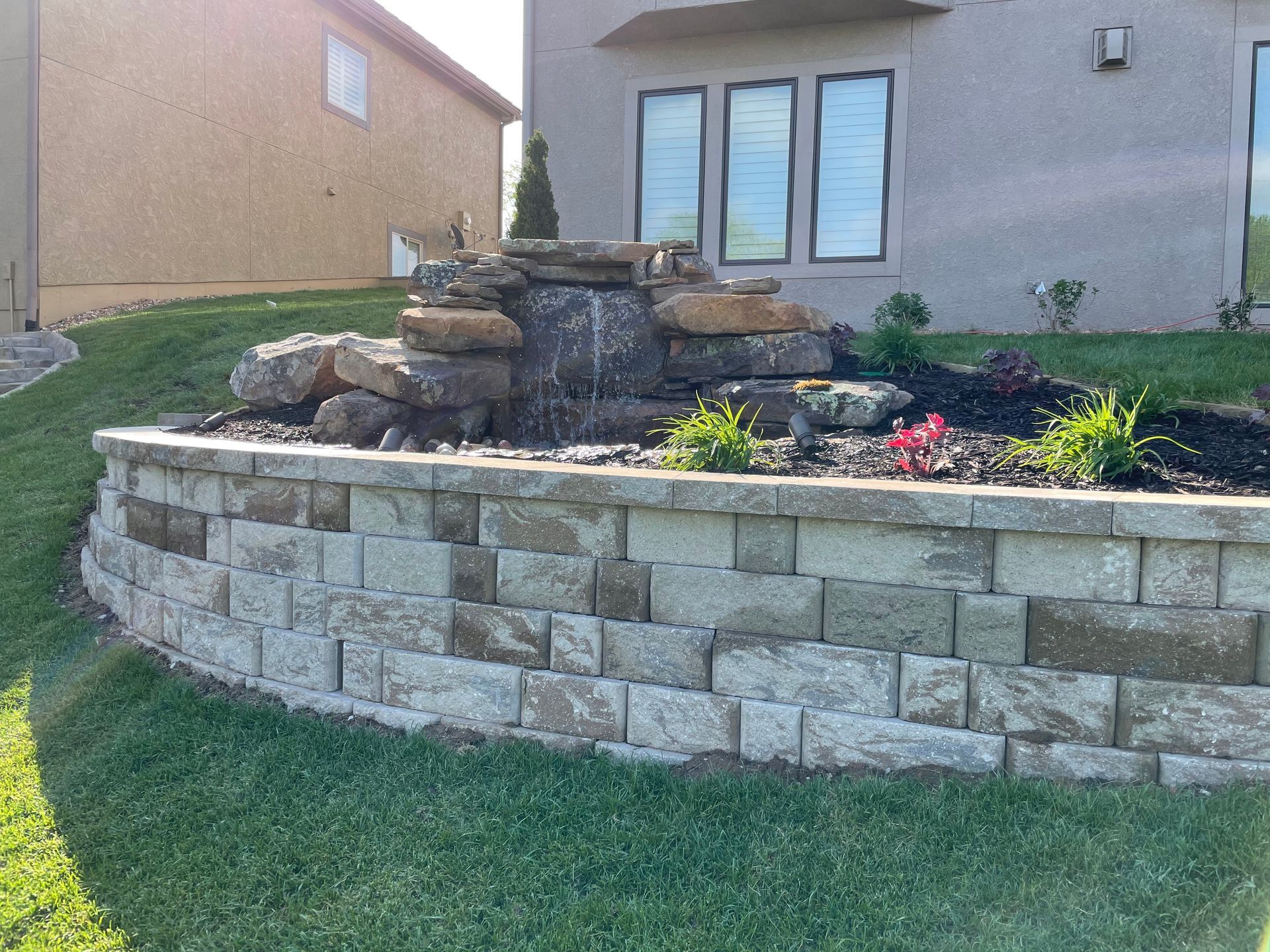 Stone retaining wall with tiered rock garden and colorful flowers in front of a house