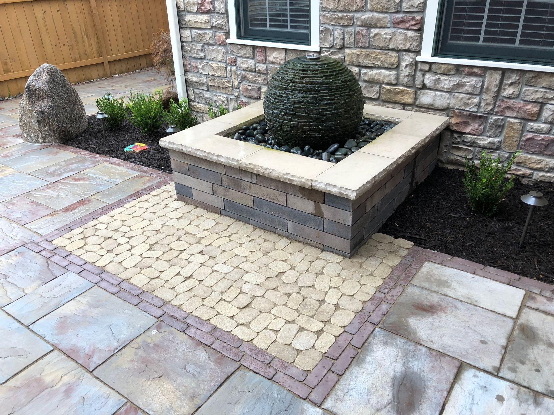 Landscaped courtyard with stone pavers and a square raised planter holding a trimmed shrub against a brick wall