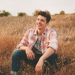 a young man is sitting in a field of tall grass and smiling