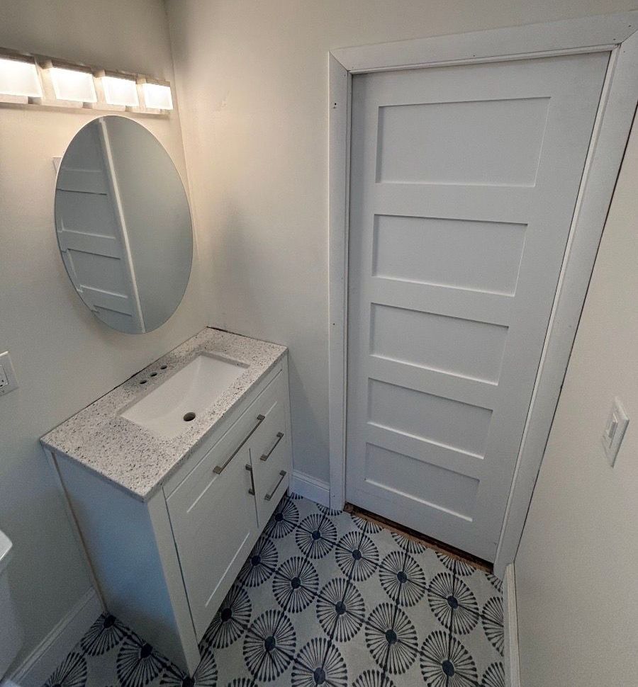 A bathroom with a sink , mirror , and door.