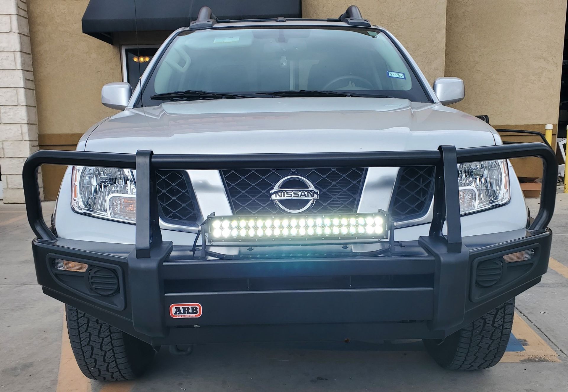 a silver nissan frontier with a black bumper is parked in a parking lot .