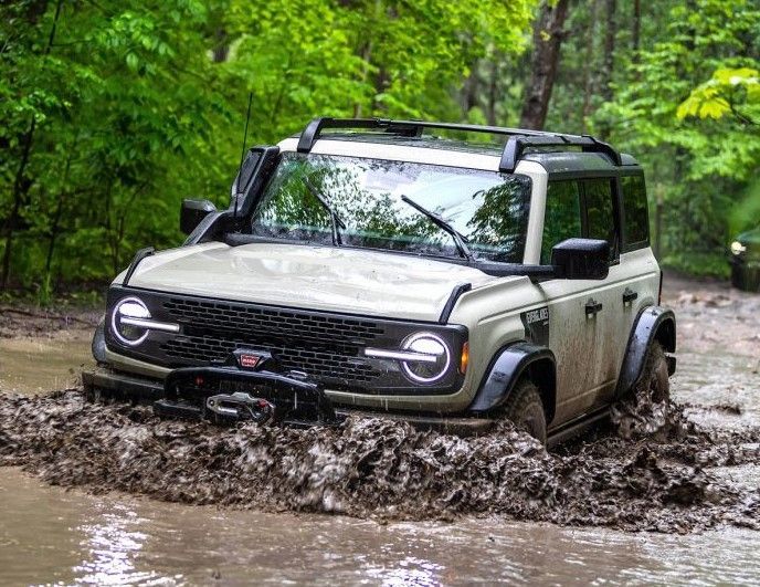 a ford bronco is driving through a muddy river .