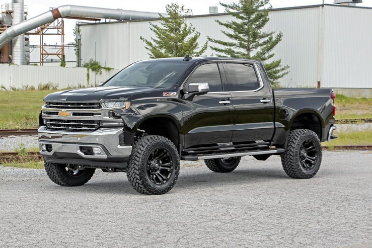a black pickup truck with a lifted body is parked on a gravel road in front of a building .