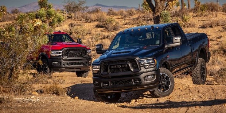 two ram trucks are driving down a dirt road in the desert .