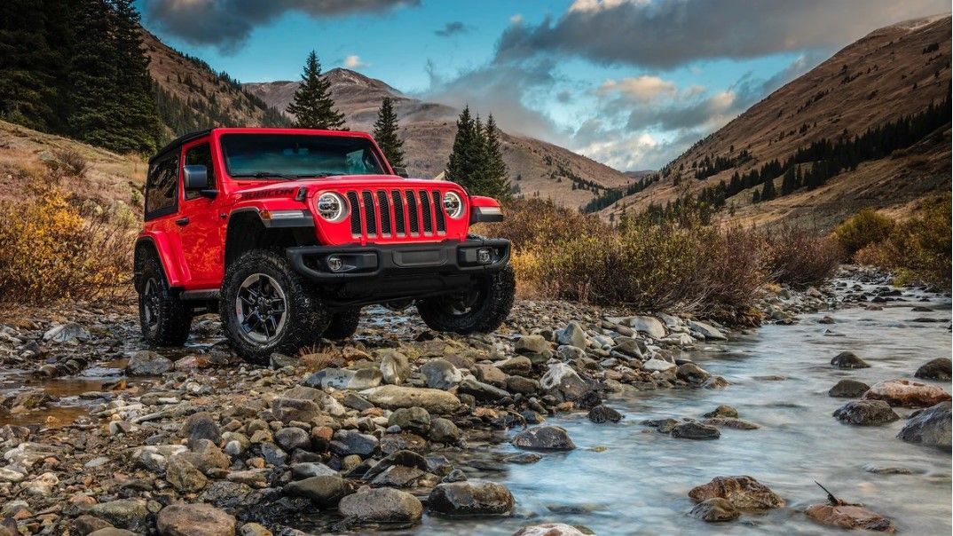 a red jeep is parked next to a river in the mountains .