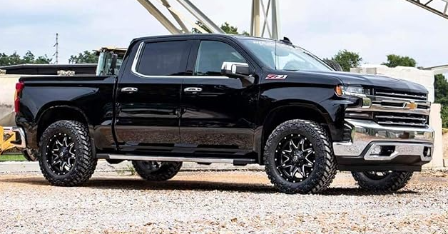 a black pickup truck is parked on gravel in front of a building .