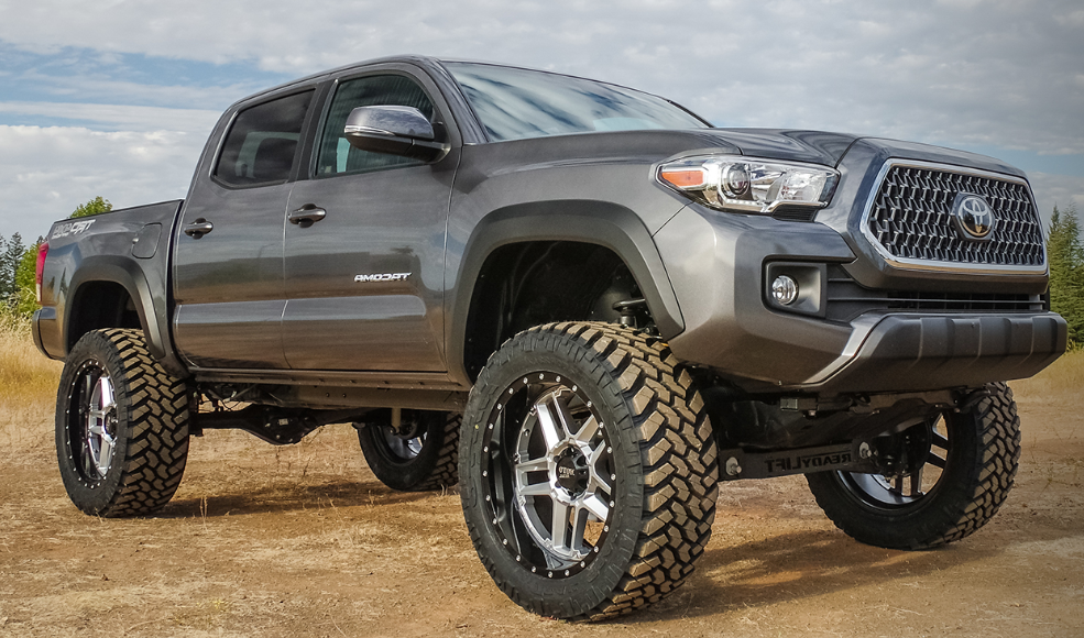 a lifted toyota tacoma pickup truck is parked on a dirt road .