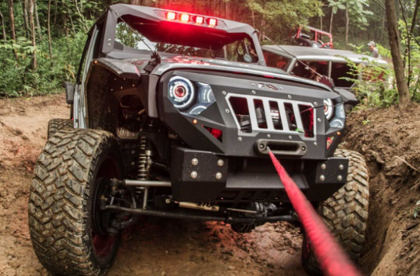 a jeep is driving down a dirt road with a winch attached to it .