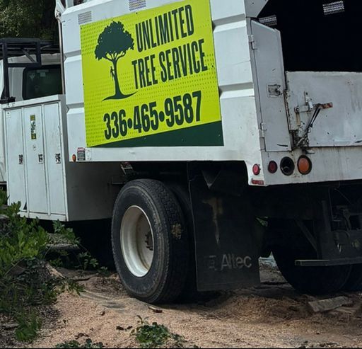 White truck with “Unlimited Tree Service” sign, phone number 336-465-9587. Outdoors, sawdust on the ground.
